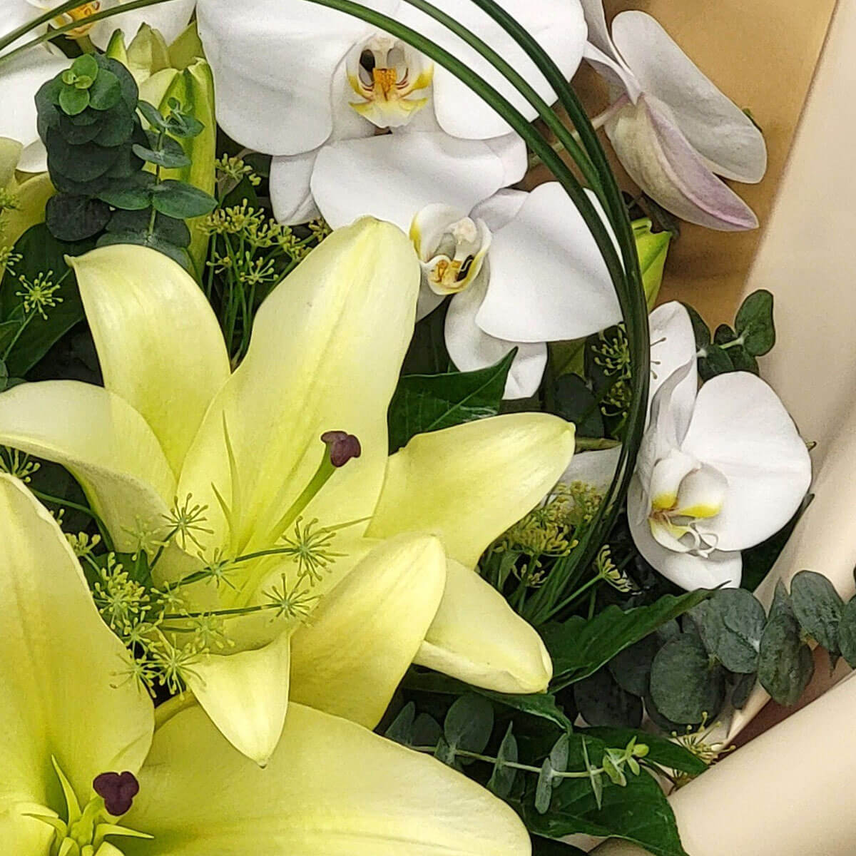 Arrangement of pale yellow lilies and white Phalaenopsis orchids with eucalyptus and textured greenery 淡黃色百合與白色蝴蝶蘭組合,搭配尤加利葉與線條感綠葉,展現高雅自然氛圍。