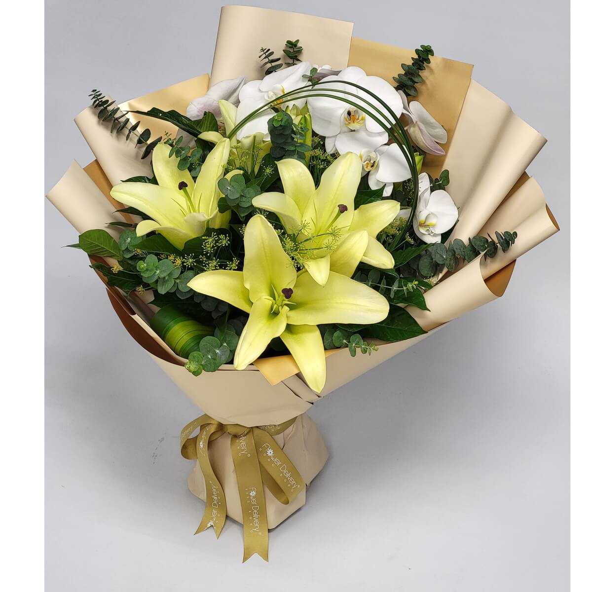 Arrangement of yellow lilies, white phalaenopsis orchids, and eucalyptus, wrapped in layered beige-gold paper and finished with a gold ribbon. 黃百合、白蝴蝶蘭配尤加利葉花束,米金雙色包裝,綁上金色絲帶。