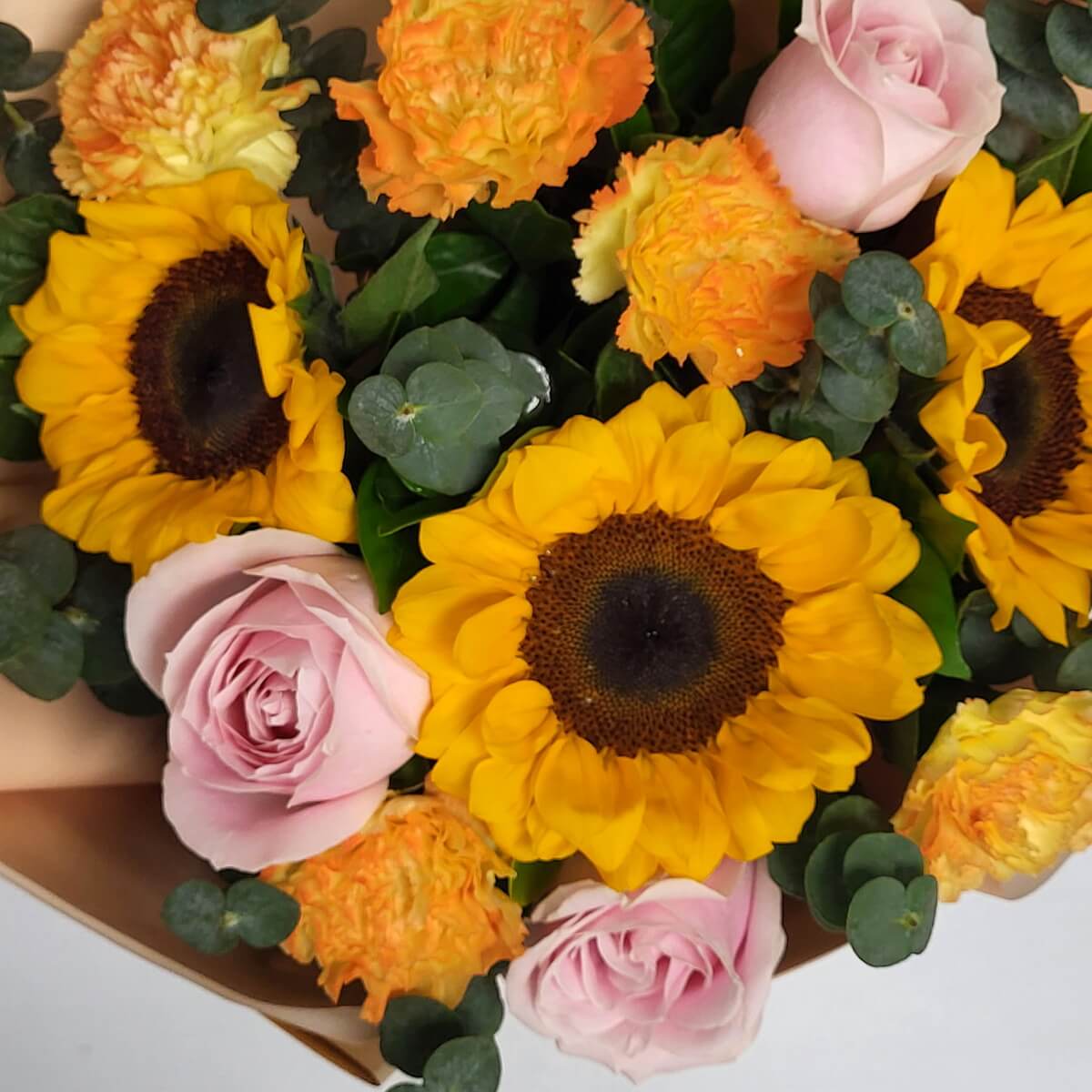 Detailed view of bright sunflowers, soft pink roses, two-tone orange carnations, and round eucalyptus foliage 鮮黃向日葵、柔粉玫瑰、橙黃漸變康乃馨與圓形尤加利葉細節近照