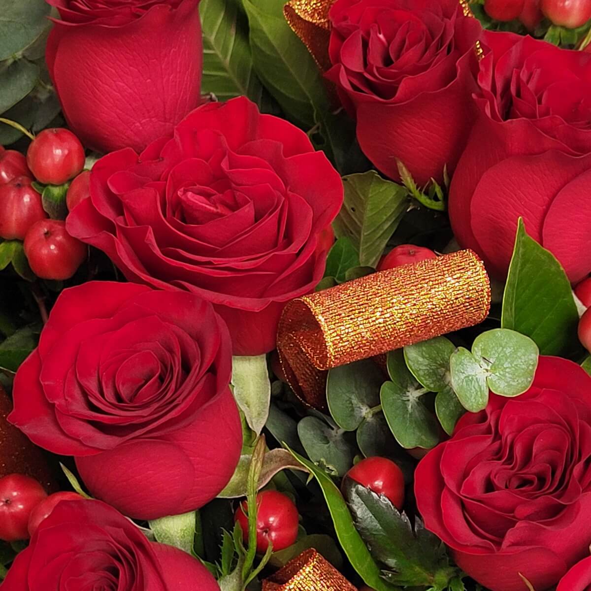 Close-up of lush red roses with red hypericum berries, gold mesh ribbon, and mixed green foliage. | 特寫飽滿紅玫瑰配紅燈籠果、金色網狀絲帶及多款綠葉。
