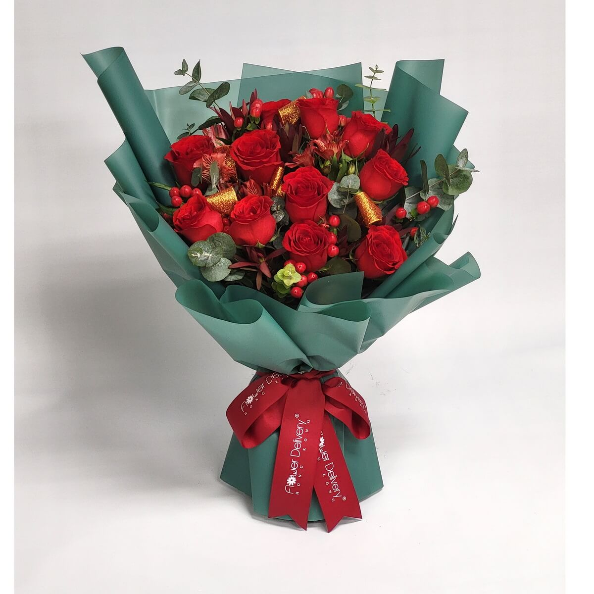 Arrangement of red roses, red hypericum berries, eucalyptus, and gold accents wrapped in dark green paper with a red ribbon. 紅玫瑰、紅冬青果、尤加利葉及金色裝飾花束,深綠包裝,綁上紅色絲帶。