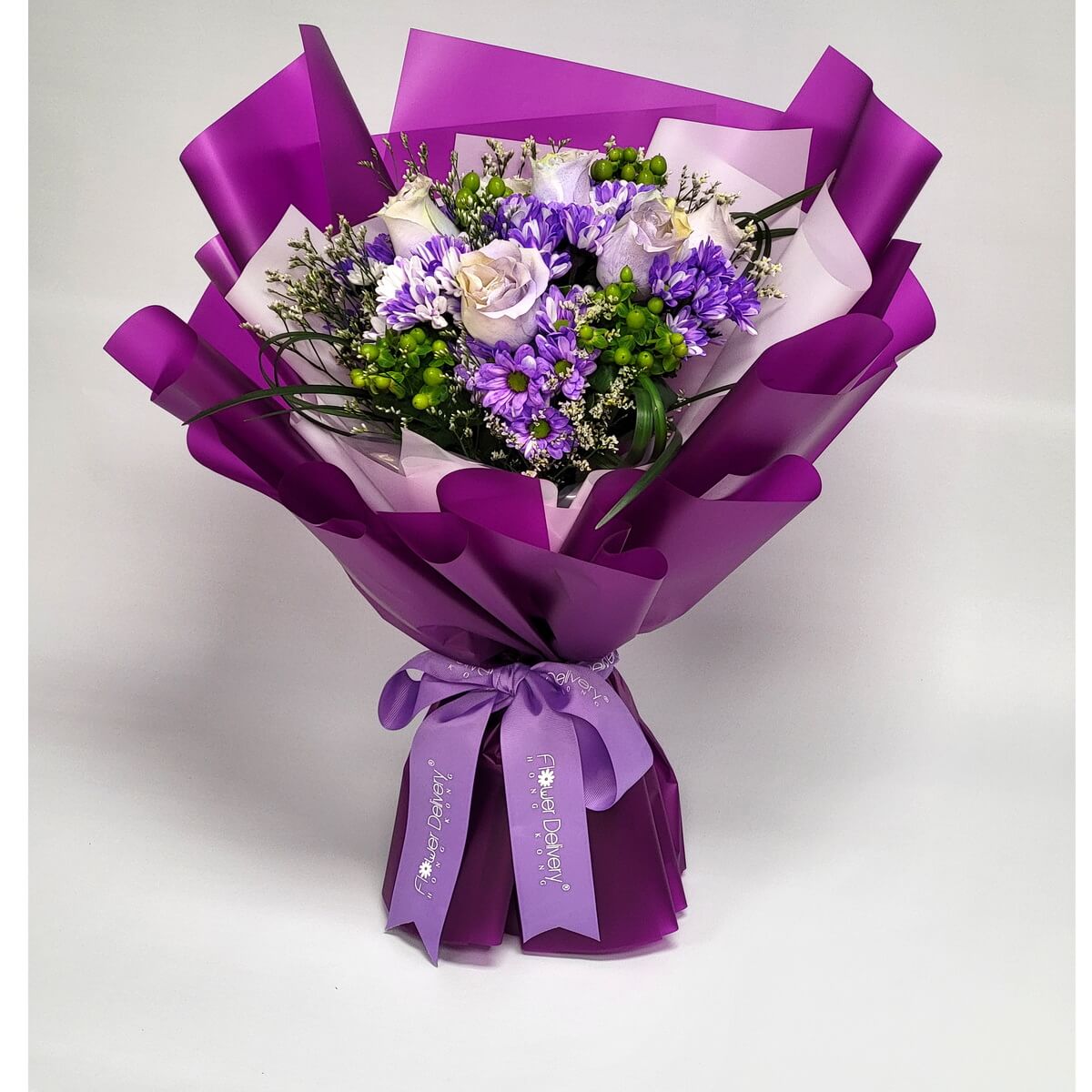 Arrangement of lavender roses, purple chrysanthemums, green hypericum berries, and filler flowers, wrapped in violet paper with a purple ribbon. 淺紫玫瑰、紫菊、綠色冬青果及襯花,紫色包裝配紫色絲帶。