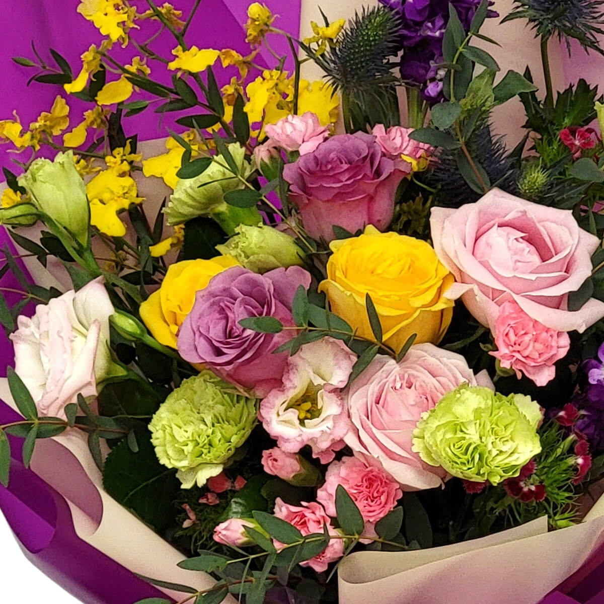 Vibrant rose bouquet with pink, yellow, and lavender blooms 粉紅、黃色與薰衣草色玫瑰交織,搭配綠色與紫色花材點綴,紫米色包裝紙提升整體優雅與浪漫感。