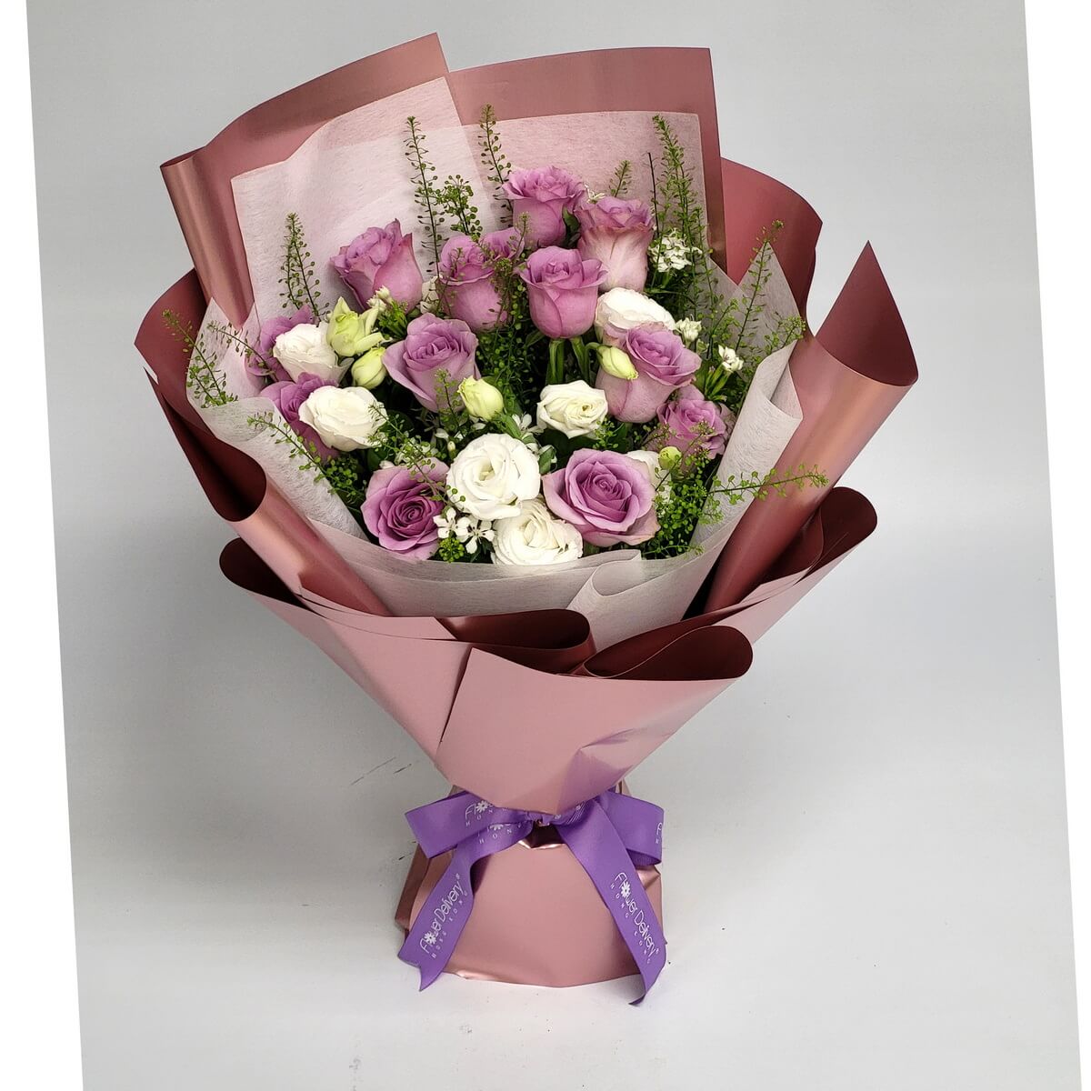 Arrangement of lavender and white lisianthus with assorted greenery, wrapped in rose gold paper and finished with a purple ribbon. 紫色與白色洋桔梗花束配綠葉,玫瑰金包裝及紫色絲帶。
