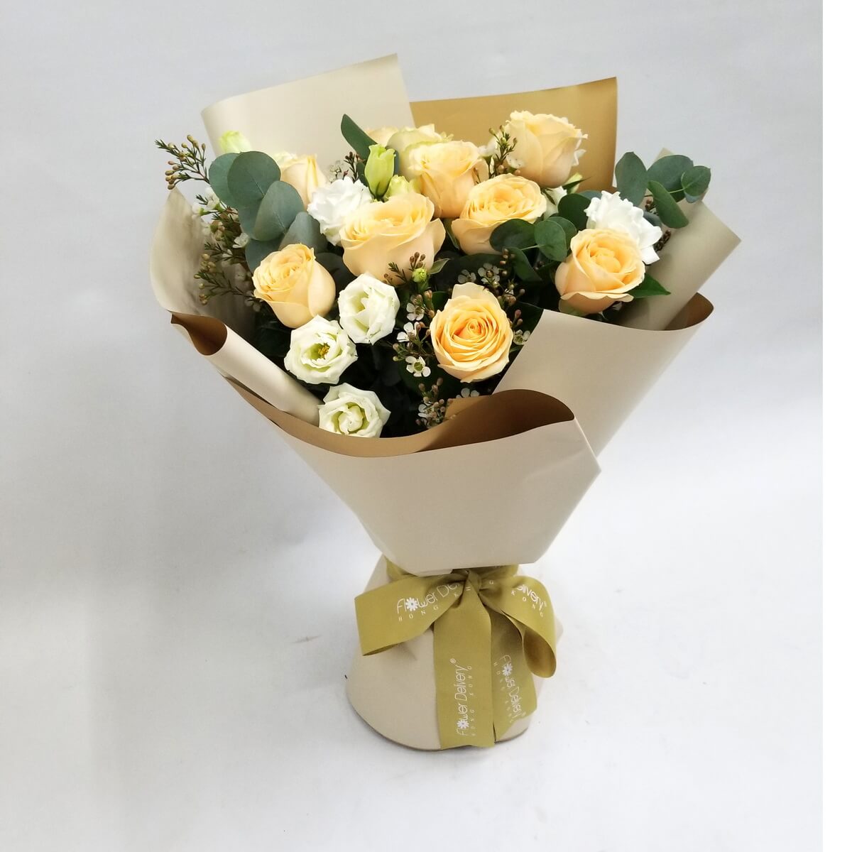 Arrangement of soft peach roses, white lisianthus, eucalyptus, and fillers wrapped in beige paper with a gold ribbon. 淡蜜桃玫瑰、白洋桔梗及尤加利葉花束,配白色襯花及金色絲帶,米白包裝。