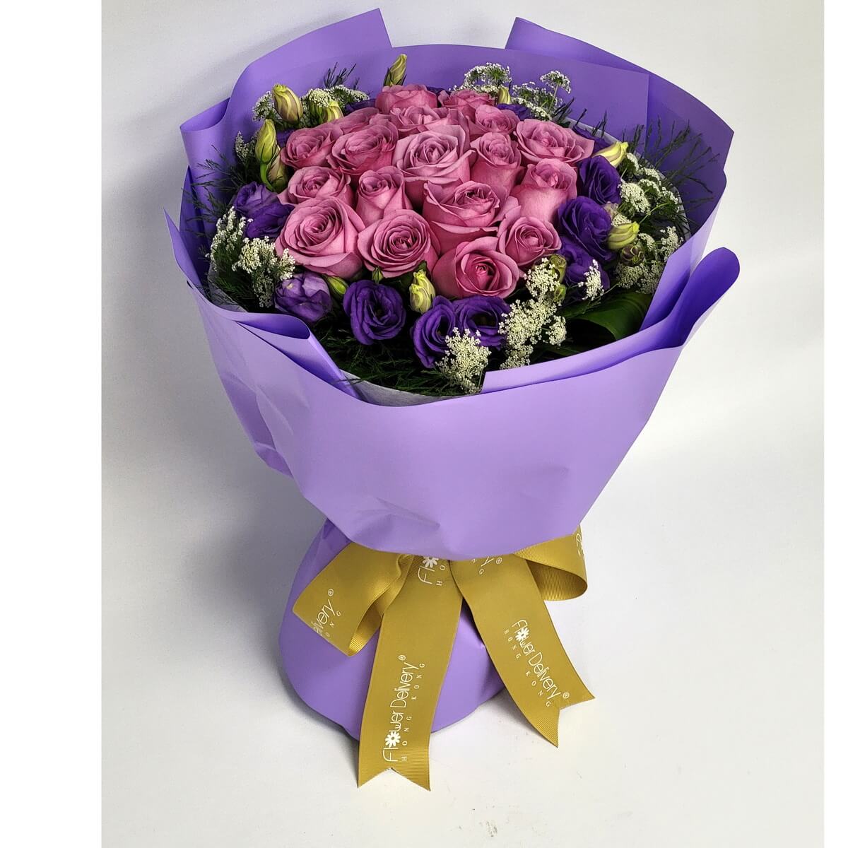 Arrangement of pink roses, purple lisianthus, and white filler flowers wrapped in lavender paper with a gold ribbon. 粉紅玫瑰、紫色洋桔梗及白色襯花,薰衣草色包裝,綁上金色絲帶。