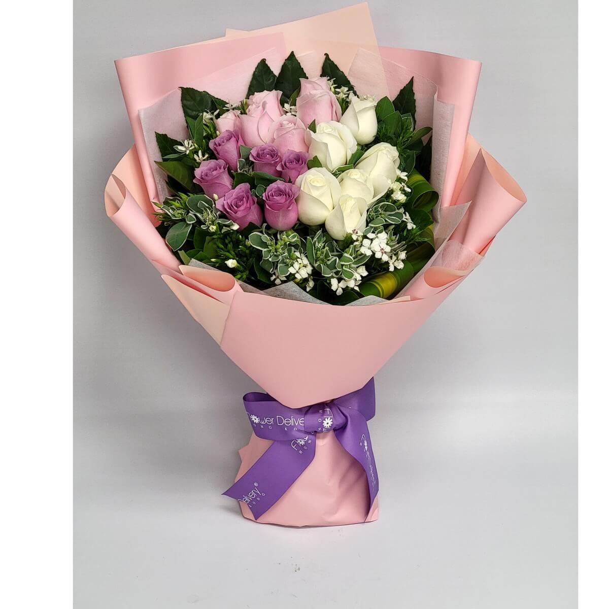 Bouquet of white, lavender, and soft pink roses accented with greenery and white filler blooms in pink wrap. 白玫瑰、紫玫瑰及粉紅玫瑰花束,配白色襯花及綠葉,粉紅包裝。
