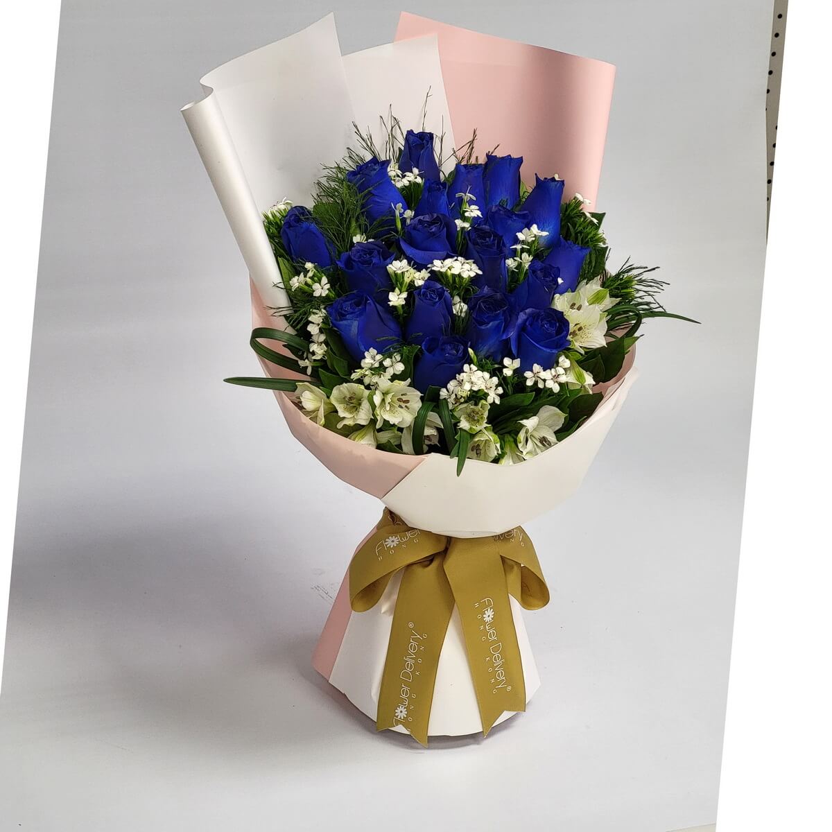 A bold bouquet of royal blue roses accented with white alstroemeria and tiny white blooms, wrapped in ivory and blush pink paper with a golden ribbon. 深藍玫瑰與白色花朵交織,展現高貴與神秘的浪漫氛圍。