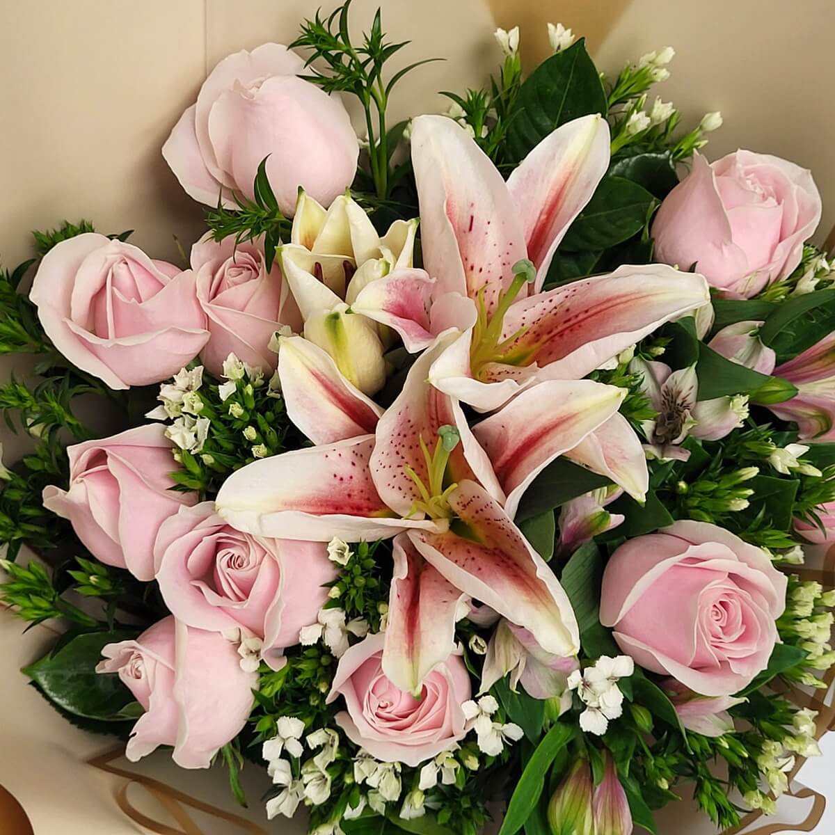 Top-down view of pink oriental lilies with spotted petals, pale pink roses, white filler blooms, and lush greenery 淡粉斑點百合、粉玫瑰、白色配花與濃綠葉材的俯視圖花束