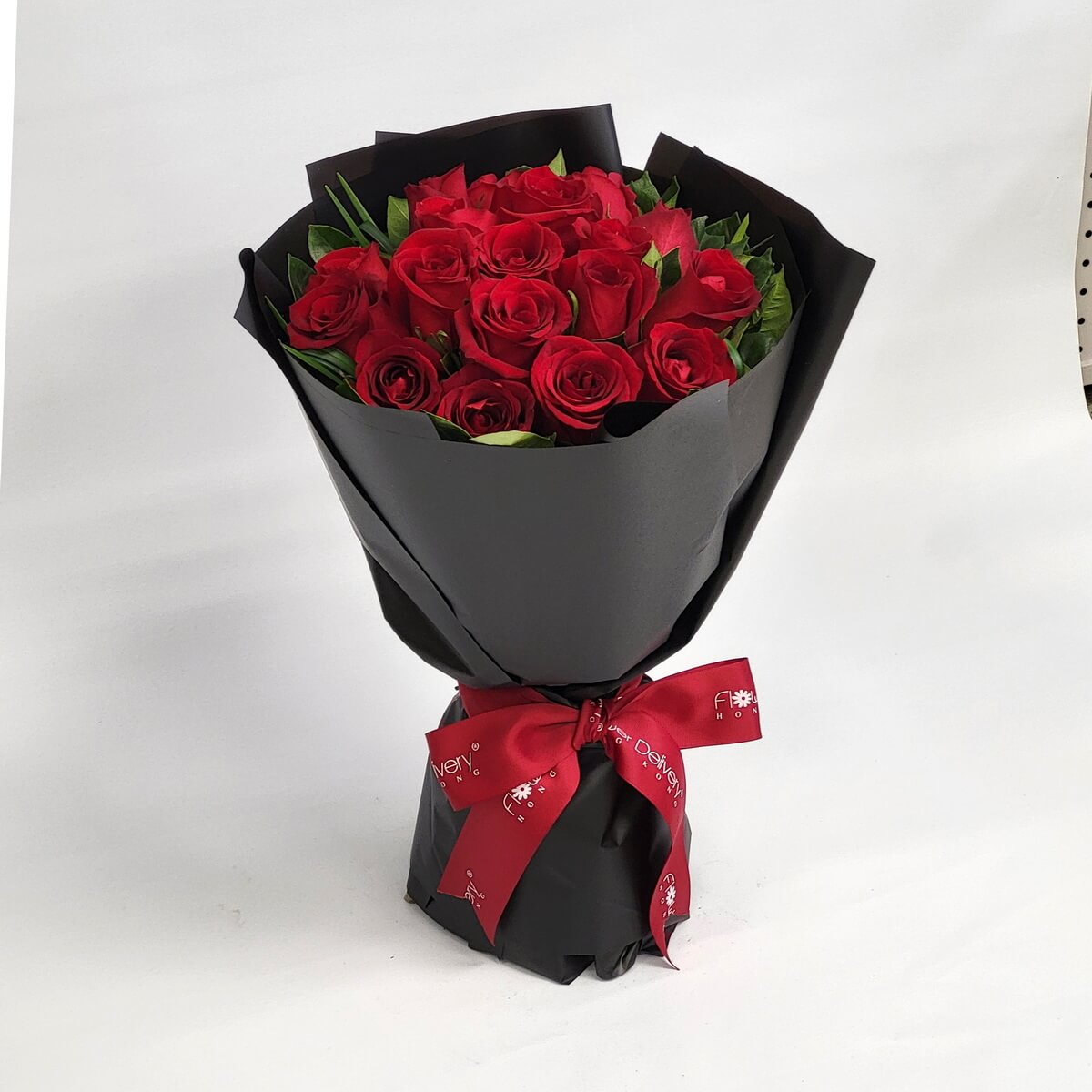 A bouquet of velvety red roses wrapped in matte black paper and tied with a red satin ribbon. 絲絨紅玫瑰搭配黑色包裝與紅緞帶,展現深夜中的熱情與浪漫。