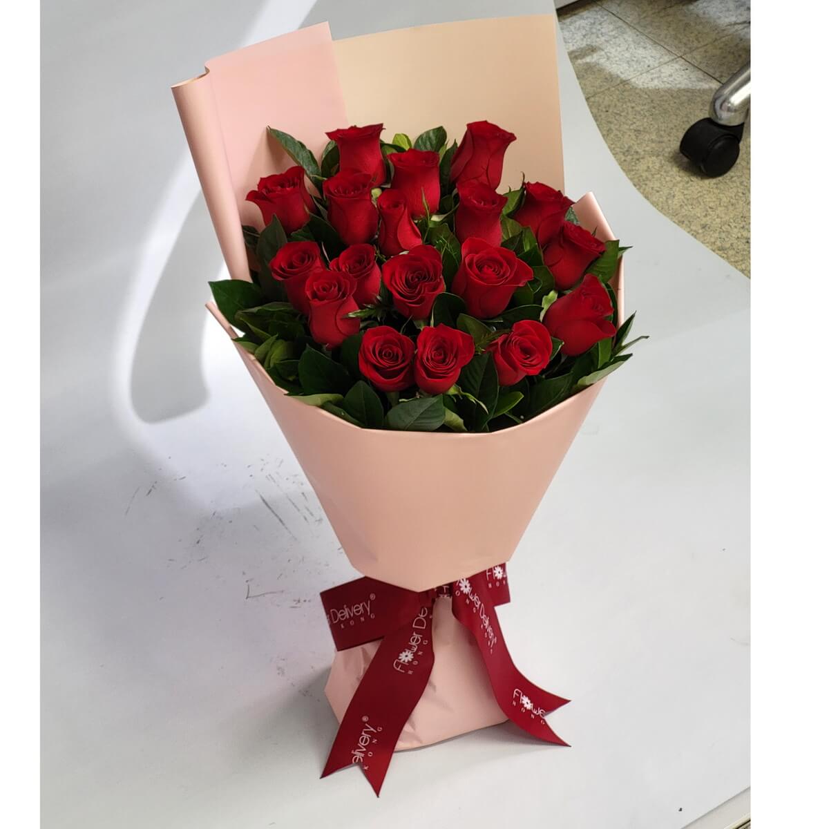 Full bouquet of long-stemmed red roses arranged with glossy green leaves, wrapped in soft pink paper and tied with a red ribbon - 長莖紅玫瑰與亮綠葉混合成束,淡粉紙包裝配紅絲帶