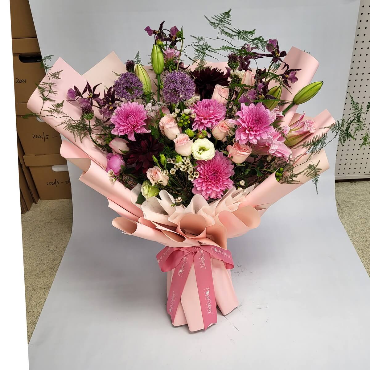 A luxurious bouquet of pink dahlias, blush roses, lisianthus, lilies, alliums, and dark plum blooms, artfully wrapped in soft blush pink paper with a matching ribbon. 柔美與神秘交織,展現高雅氣質與浪漫層次。