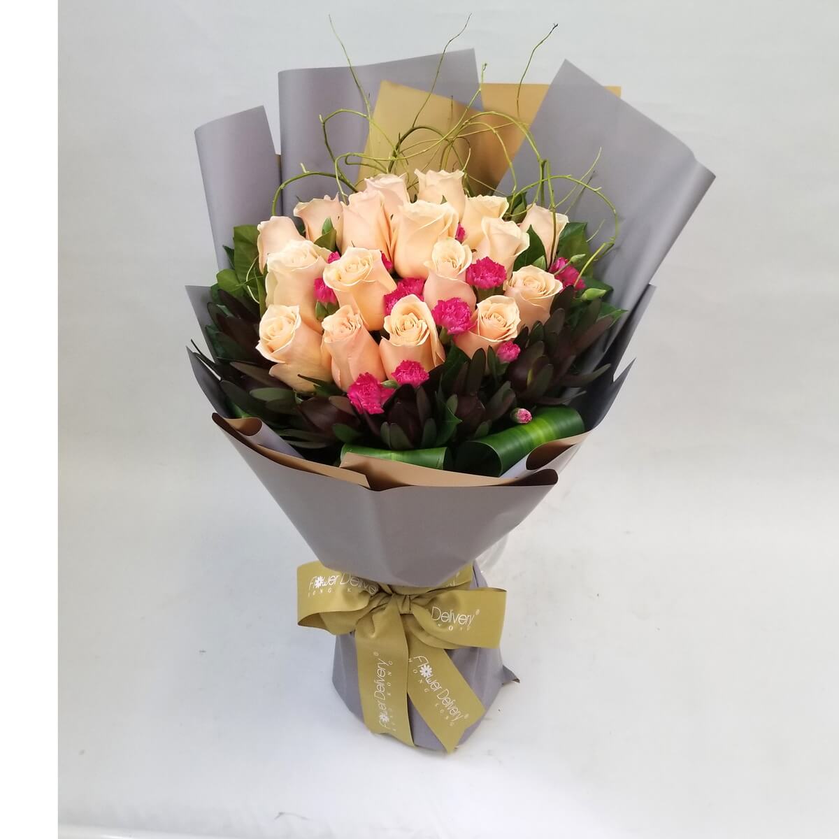 A graceful bouquet of champagne roses accented with deep pink mini carnations and lush foliage. Wrapped in muted gray and brown paper, tied with a golden ribbon. 香檳玫瑰與洋紅小花相映成趣,柔和中展現亮眼氣質。