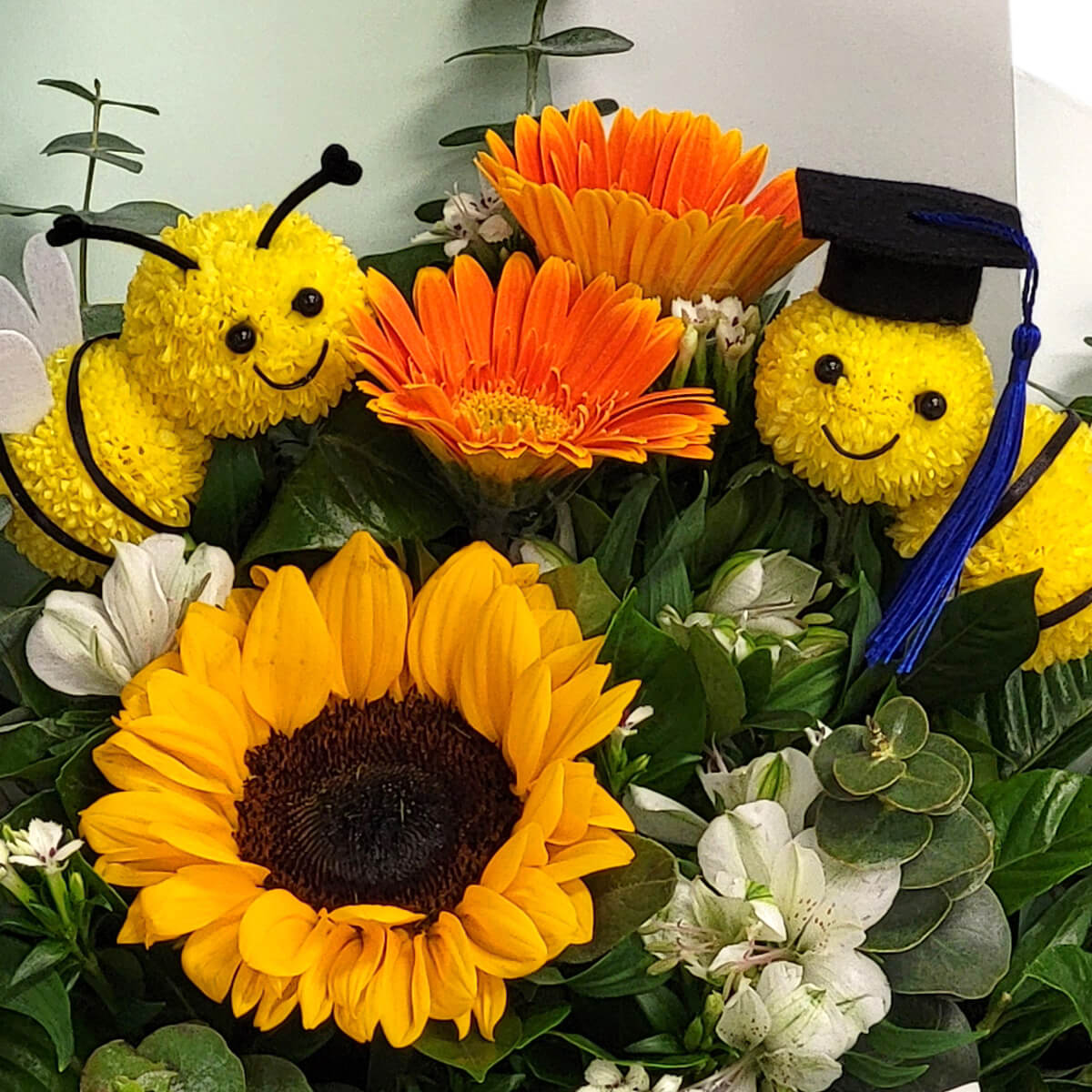 A bright sunflower bouquet with two adorable bee figures—one proudly wearing a graduation cap 向日葵搭配俏皮蜜蜂花偶,畢業帽點綴其上,象徵榮耀與嶄新旅程。