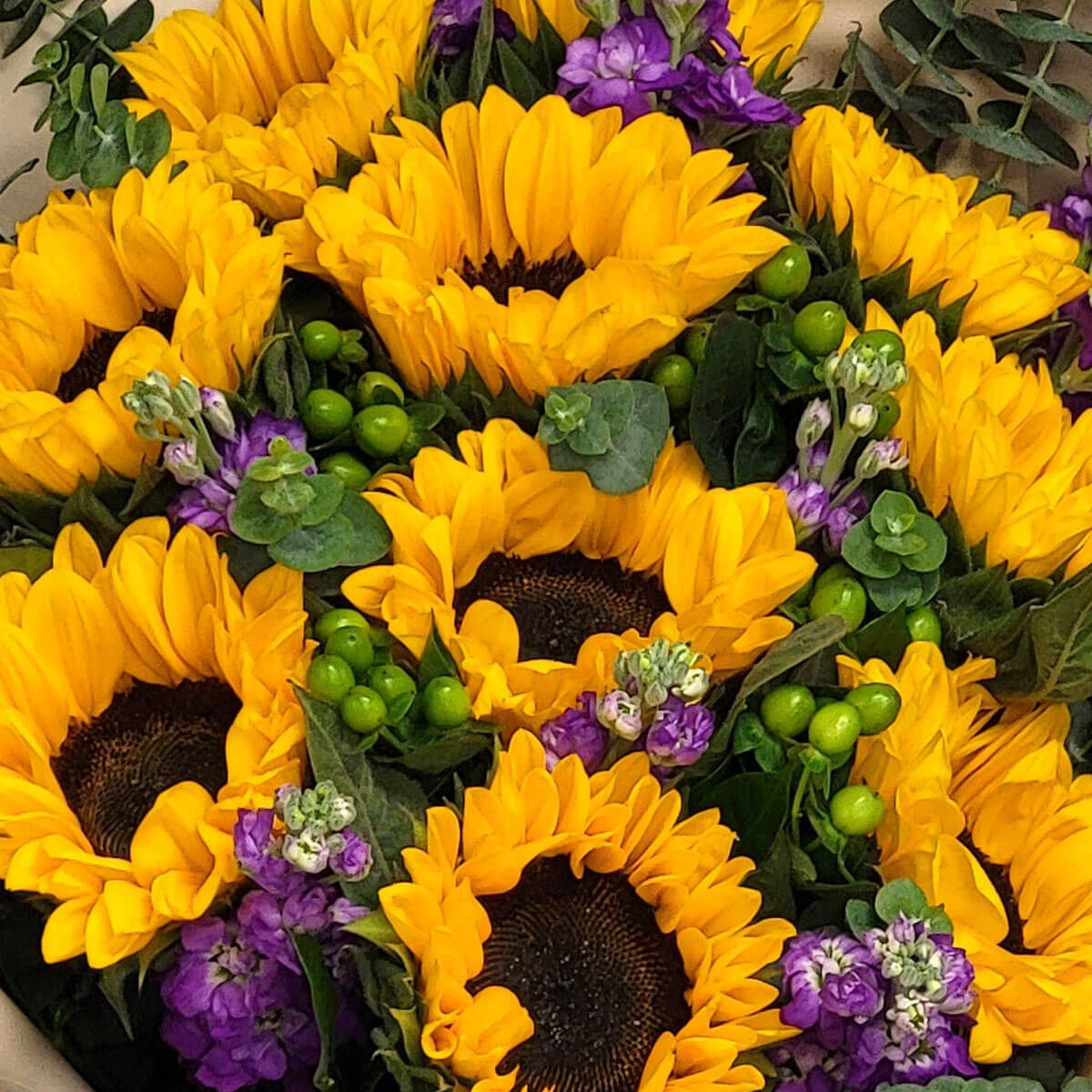 Golden sunflowers burst with sunshine energy, paired with purple flowers and fresh greenery 明亮向日葵與紫花相映成趣,綠葉與漿果點綴,展現盛夏般的熱情與生機。