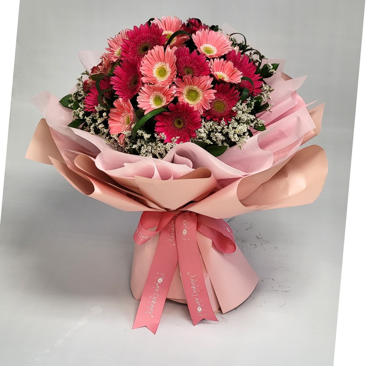 Vibrant bouquet of dark pink and peach gerberas with baby’s breath, wrapped in layered pink wrapping and tied with a pink ribbon. 粉紅與桃紅太陽花搭配滿天星,粉嫩包裝洋溢朝氣與喜悅。