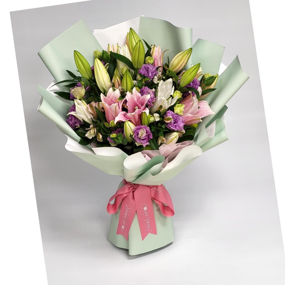 Bouquet of pink and white lilies, purple eustomas, and lush greenery wrapped in mint green and white paper with a pink ribbon. 百合與桔梗花相映成趣,清新綠白包裝搭配粉紅絲帶,展現優雅氣質。
