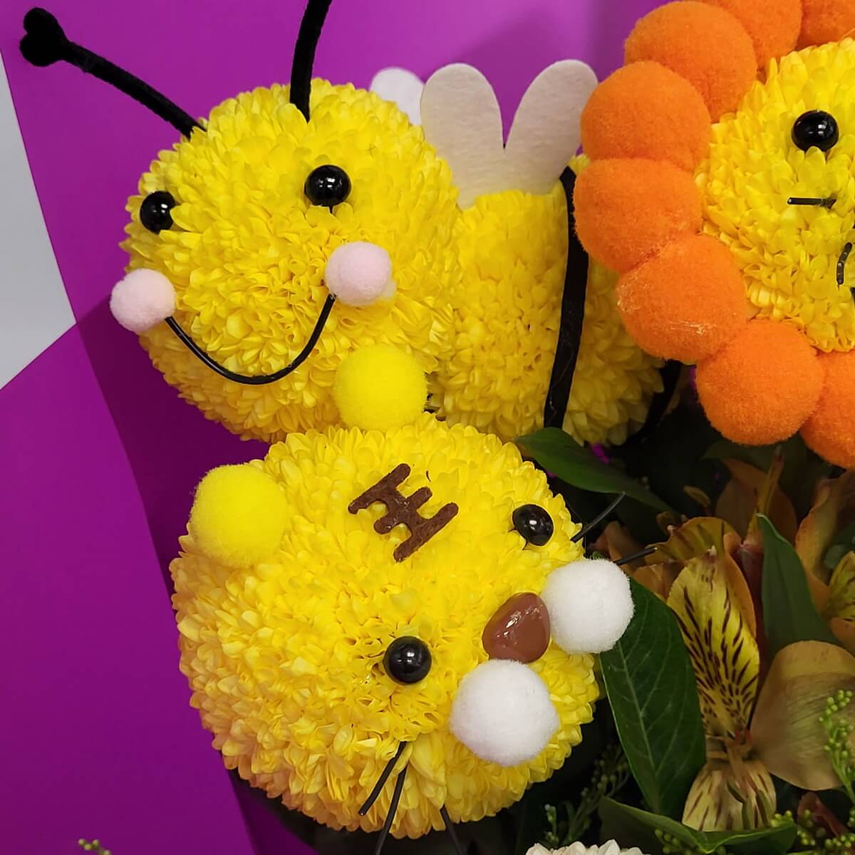 Detail view of bee and tiger characters made from yellow button chrysanthemums, featuring black antennas, felt wings, pom-pom cheeks, and decorative eyes - 黃乒乓菊製蜜蜂與老虎造型,配黑觸角、氈質翅膀、毛球面頰及裝飾眼睛特寫