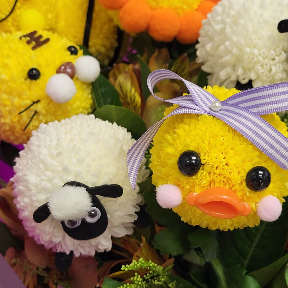 Adorable duck with orange plastic beak, pink pom-pom cheeks, and purple ribbon bow beside a white sheep with black felt face, both made from button chrysanthemums - 橙色塑膠嘴粉紅面頰小鴨與黑臉白羊,皆以乒乓菊製作,造型可愛