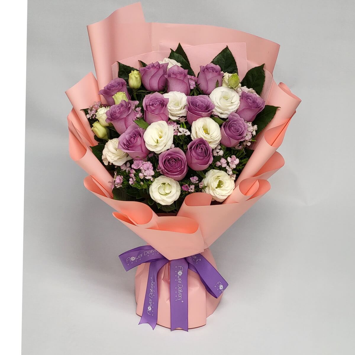 Full floral bouquet composed of lavender roses and white lisianthus, accented with delicate pink dianthus flowers, arranged densely with green foliage and finished in soft peach wrapping 紫色玫瑰與白色洋桔梗配粉紅石竹花束包裝