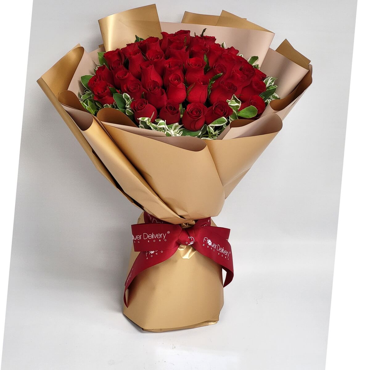 A grand bouquet of lush red roses, tightly arranged and accented with variegated greenery. Wrapped in luxurious champagne gold and beige paper, tied with a deep red ribbon. 經典紅玫瑰花束,搭配香檳金包裝,傳達濃烈愛意與尊貴氣息。