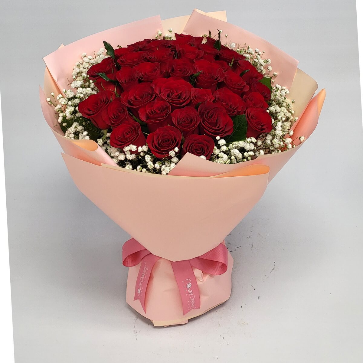 Full bouquet of velvety red roses surrounded by baby's breath and wrapped in soft blush pink paper with satin ribbon 絲絨紅玫瑰與滿天星組成的飽滿花束,柔粉包裝配緞帶完成優雅造型