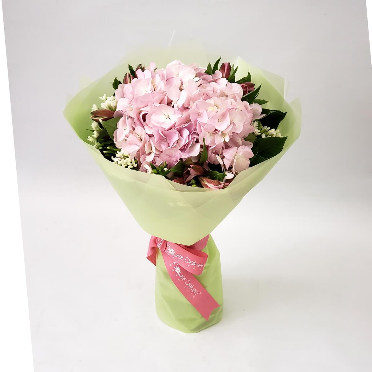 Soft pink hydrangeas surrounded by dark green foliage and white accent flowers, wrapped in pastel green paper with a pink ribbon. 粉色繡球花搭配嫩綠包裝,簡約清新,洋溢自然溫柔。