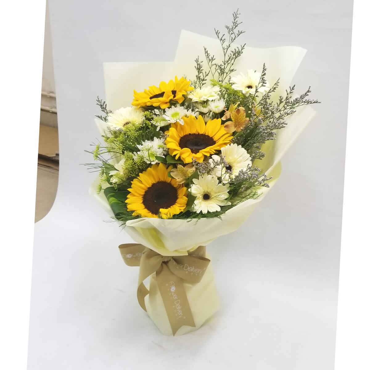 A bright bouquet of sunflowers and cream gerberas, accented with yellow daisies and green fillers, wrapped in soft pale yellow paper and tied with a golden ribbon. 向日葵與奶油色太陽花交織,黃白相映,清新自然,散發暖陽氣息。