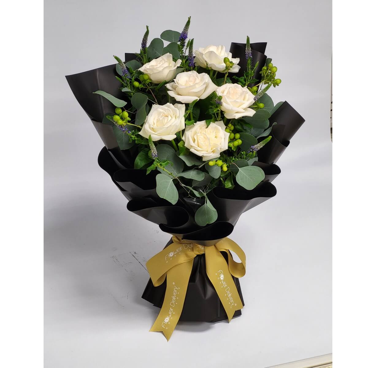 Elegant white roses paired with eucalyptus and green berries, wrapped in striking black paper and tied with a golden ribbon. 優雅白玫瑰與綠色果實搭配,黑色包裝突顯純白花朵之美,綴以金絲帶,氣質非凡。