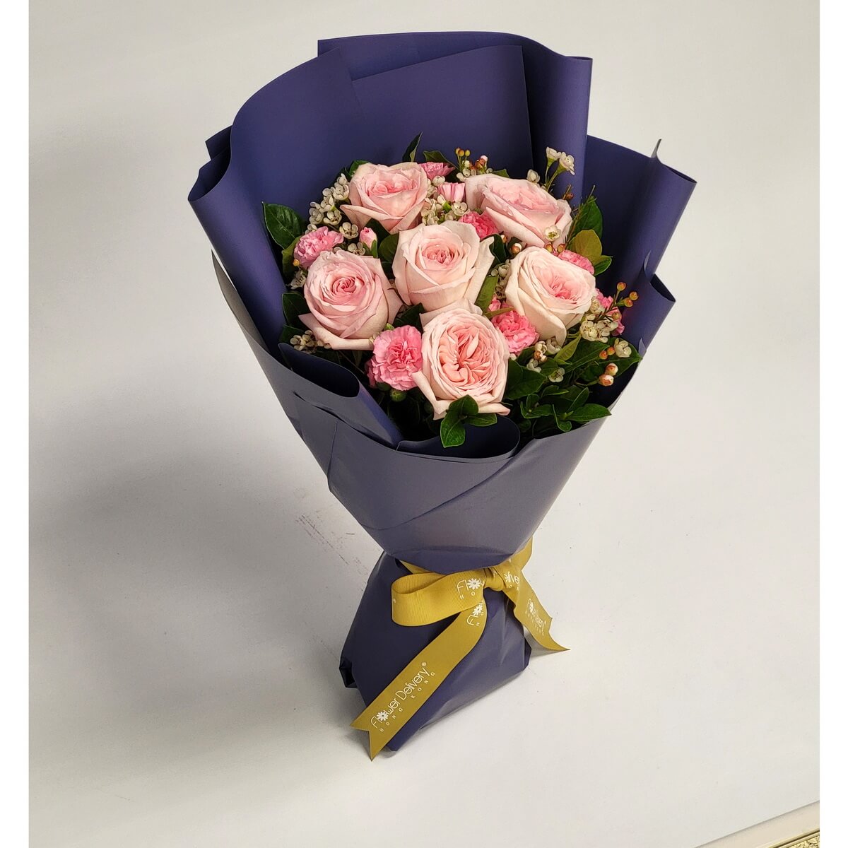 Elegant bouquet of blush pink roses and mini carnations, accented with berries and buds. Wrapped in royal purple paper with a golden yellow ribbon. 粉紅玫瑰與小康乃馨搭配深紫包裝與金黃絲帶,展現優雅與溫柔。