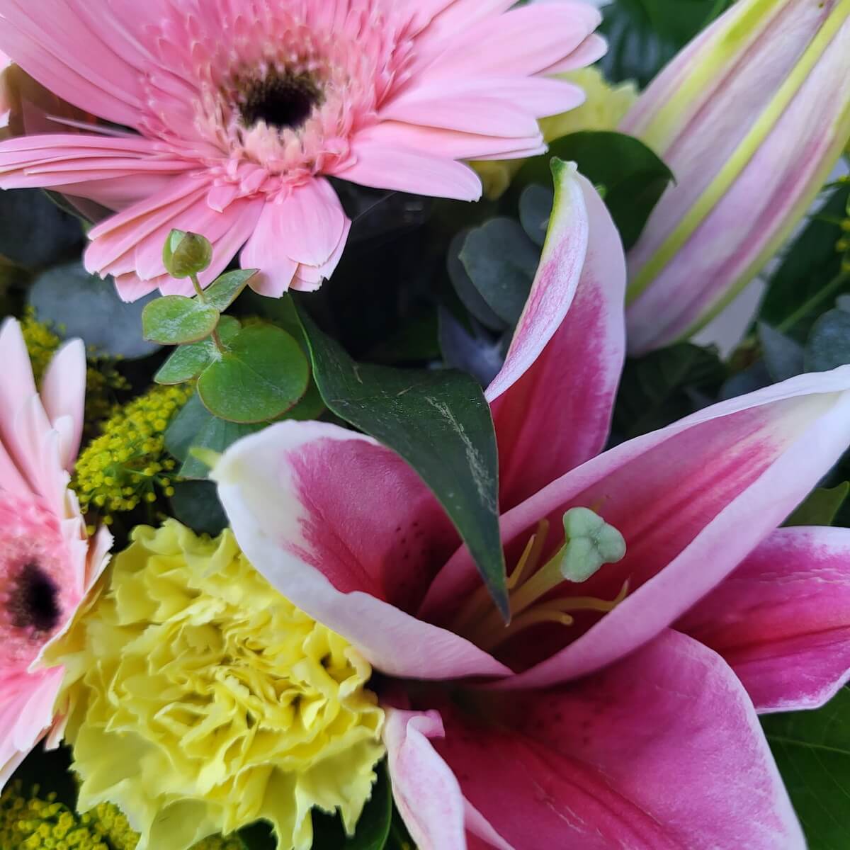Macro view of pink gerbera, yellow carnation, and open pink lily with bud and green foliage | 粉紅非洲菊、黃康乃馨與盛放粉紅百合特寫,配搭花苞與濃綠葉材,色彩對比鮮明自然。