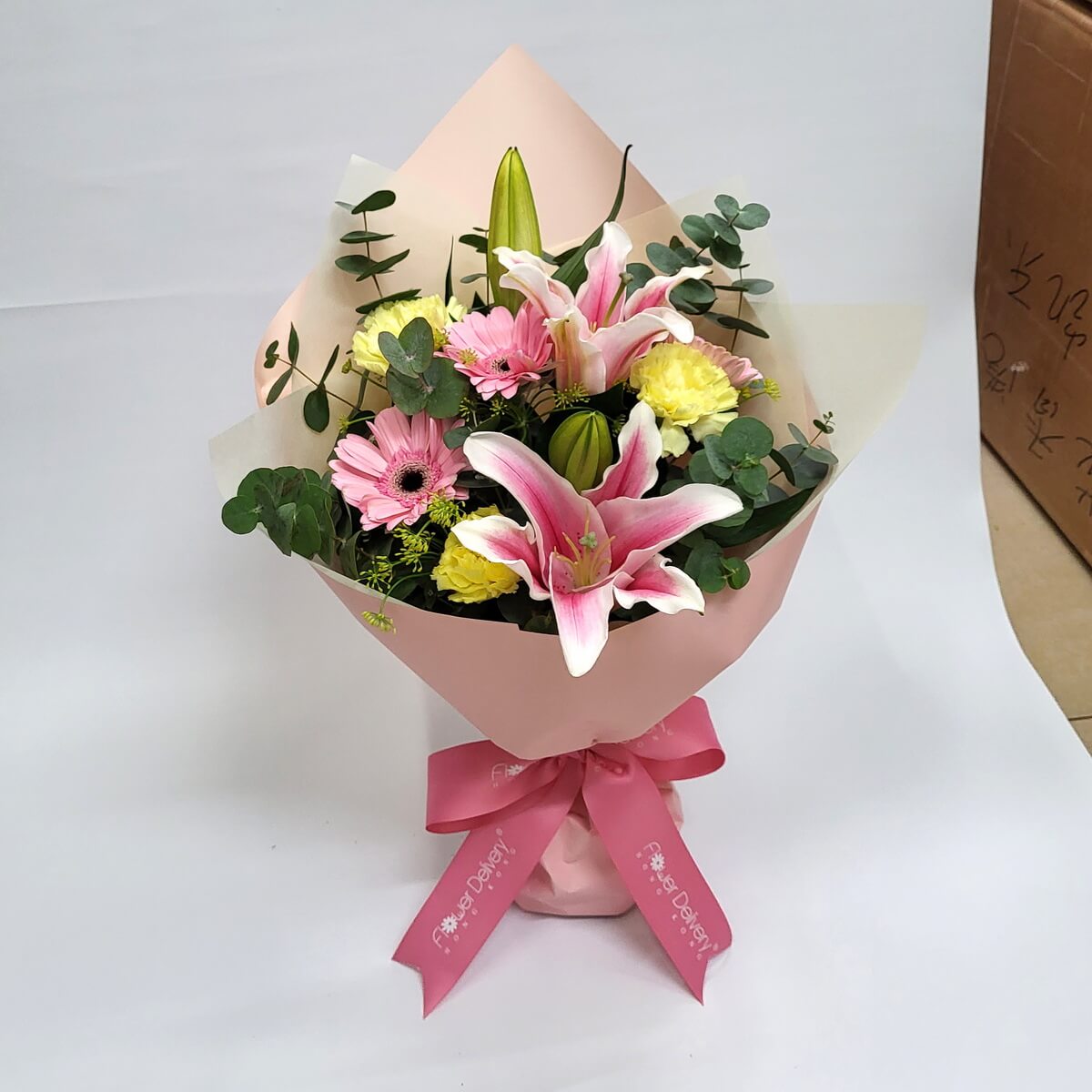 Soft pink lilies and gerberas with yellow carnations, wrapped in blush pink paper and tied with a matching ribbon. A fresh and joyful bouquet. 粉紅百合與黃康乃馨花束,粉包裝與蝴蝶結展現青春氣息。