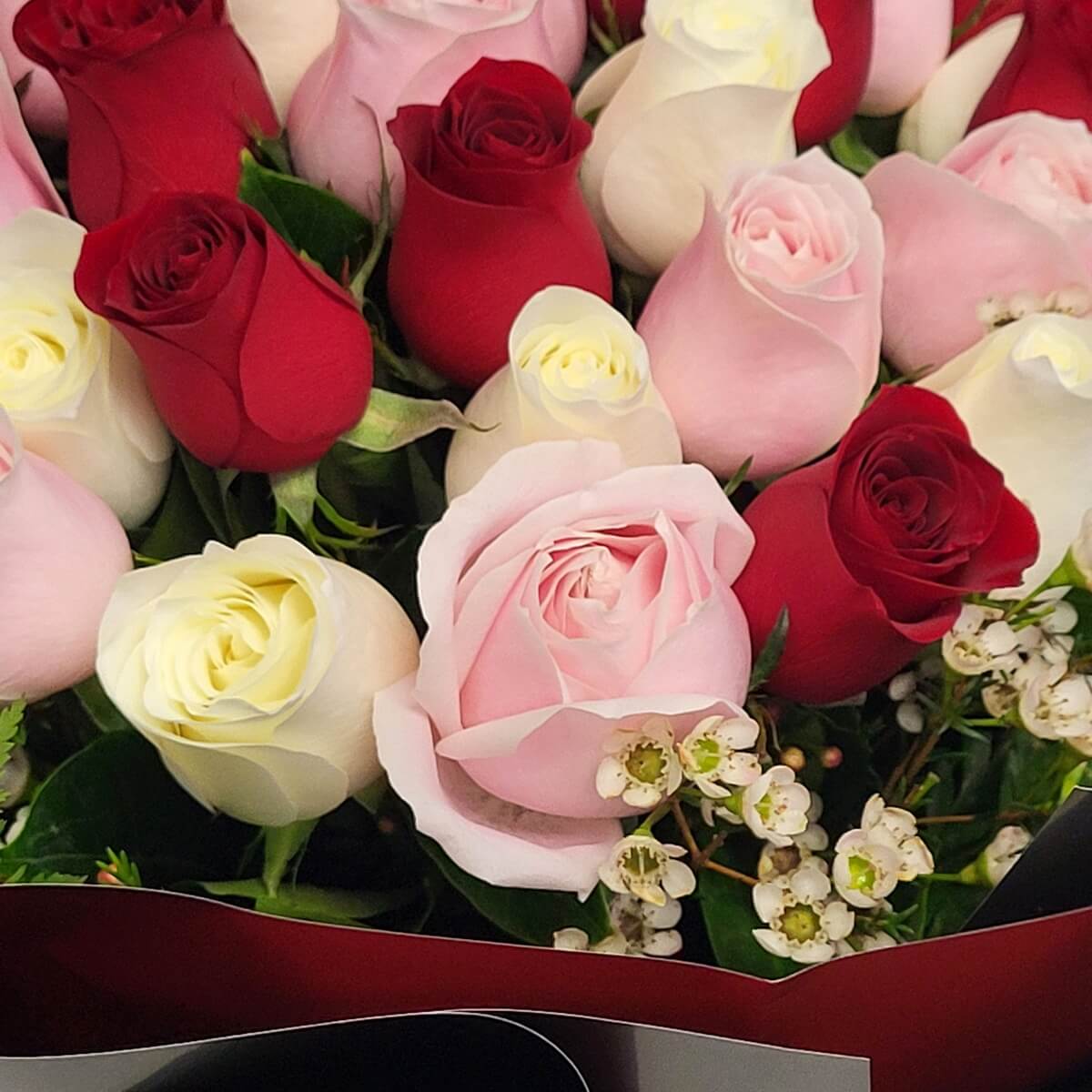 Close-up featuring mixed red, blush pink, and cream roses with sprigs of white waxflower for soft contrast 紅、粉與奶白玫瑰交錯,配以白蠟梅小花點綴,構成柔和對比的特寫畫面