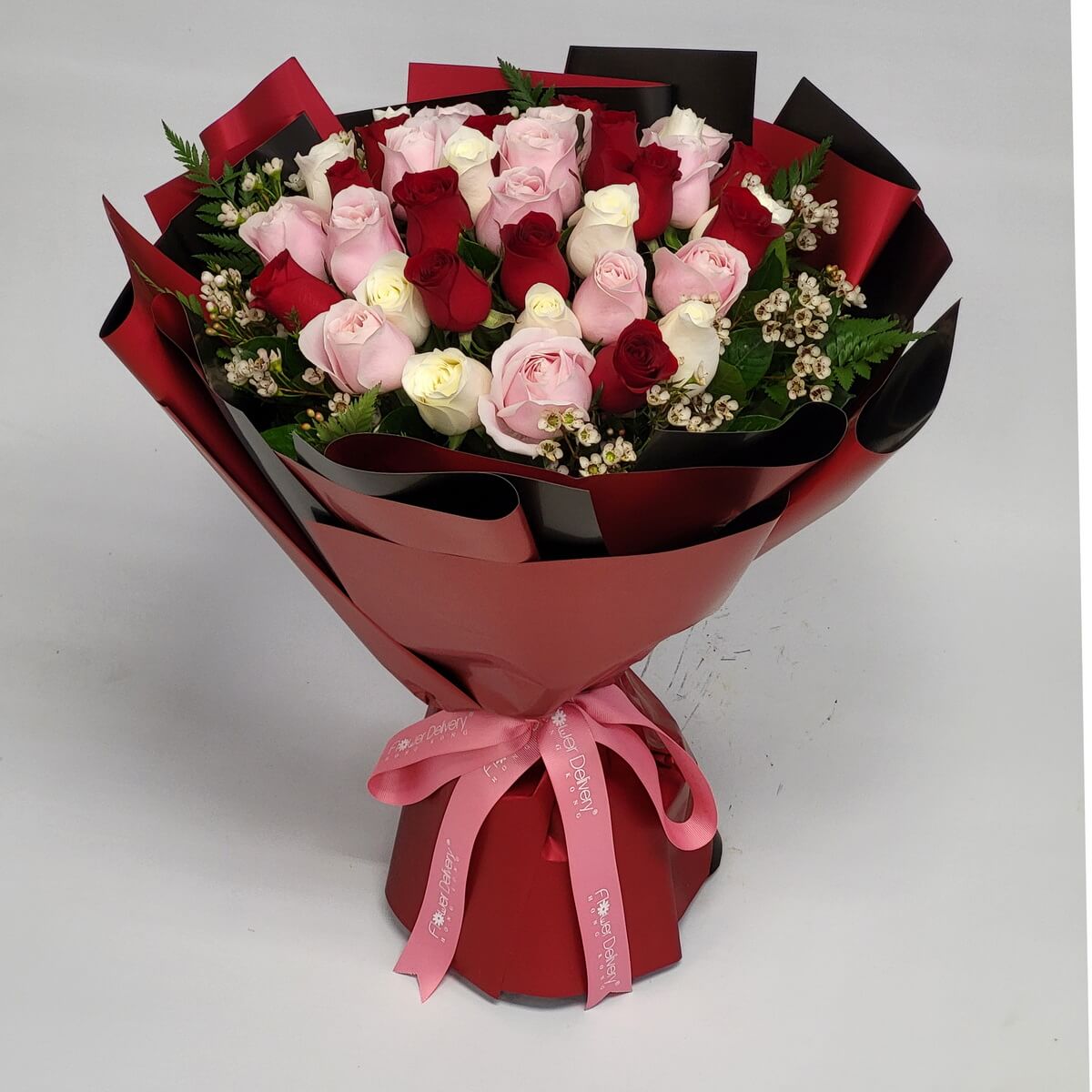 Elegant hand-tied bouquet featuring red, pink, and cream roses with sprigs of waxflower, wrapped in structured deep red paper and pink ribbon 經典紅、粉與奶白玫瑰花束,配蠟梅及深紅包裝紙與粉紅絲帶優雅呈現