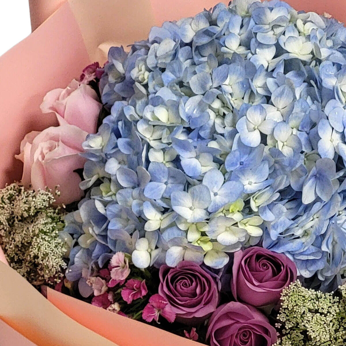 Cloud-like blue hydrangeas with lavender roses and dainty pink accents, wrapped in soft peach hues 雲朵般的藍繡球與紫玫瑰、粉色小花組成夢幻花束,溫柔迷人。