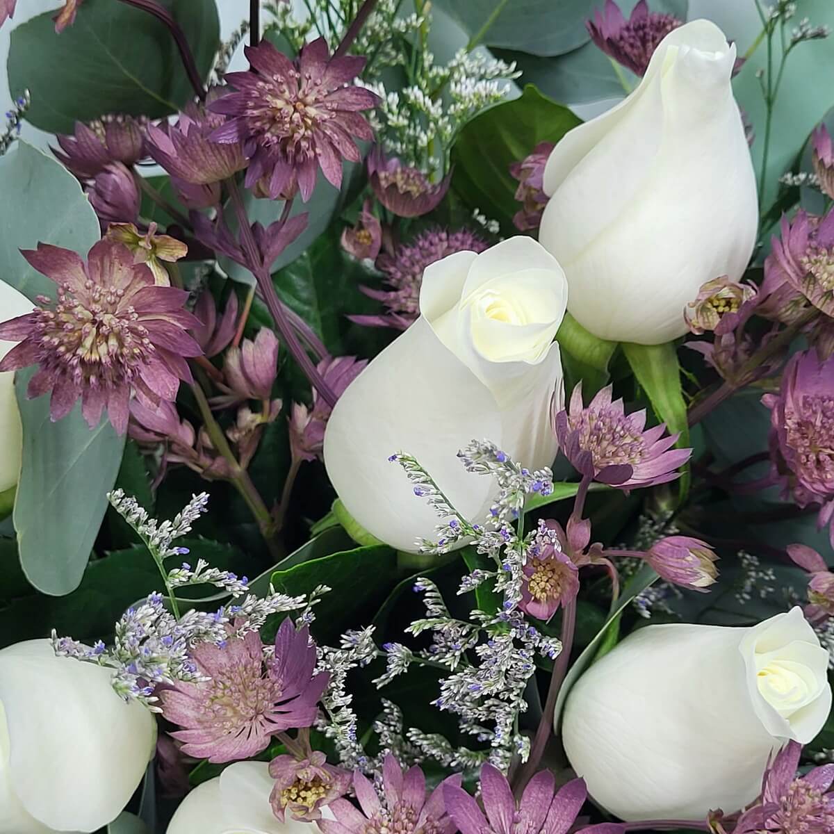 Detail view of ivory roses arranged with dusty mauve astrantia, sprigs of purple limonium, and layered green and silver foliage 象牙白玫瑰、粉紫星狀花、紫情人草與層次分明的綠銀葉材構成的細緻特寫構圖