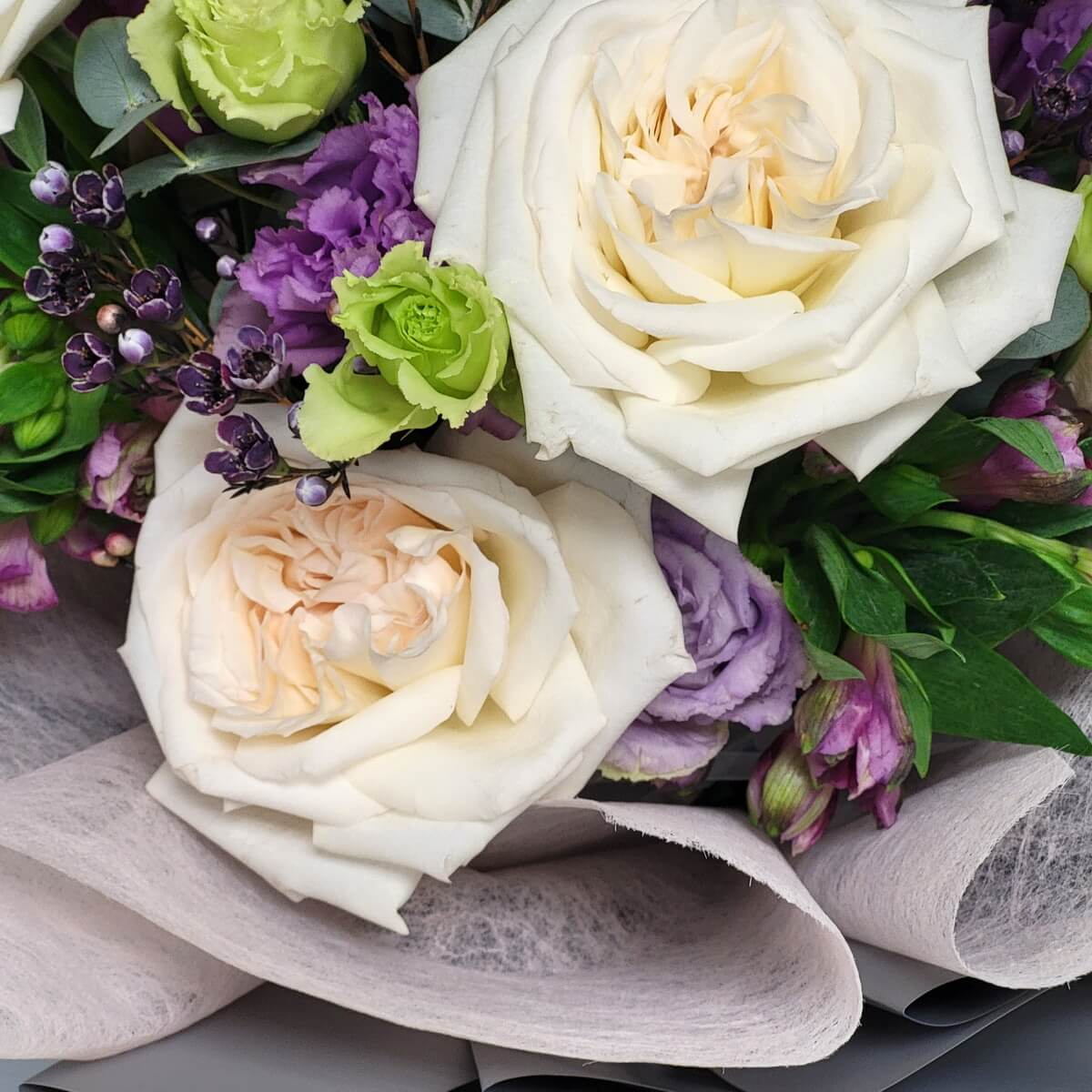 Detail view of creamy white garden roses paired with green and purple lisianthus, dark purple wax flowers, and fresh greenery wrapped in pale mesh - 奶白玫瑰配綠紫洋桔梗、深紫蠟花及新鮮綠葉,淡粉網布包裝特寫