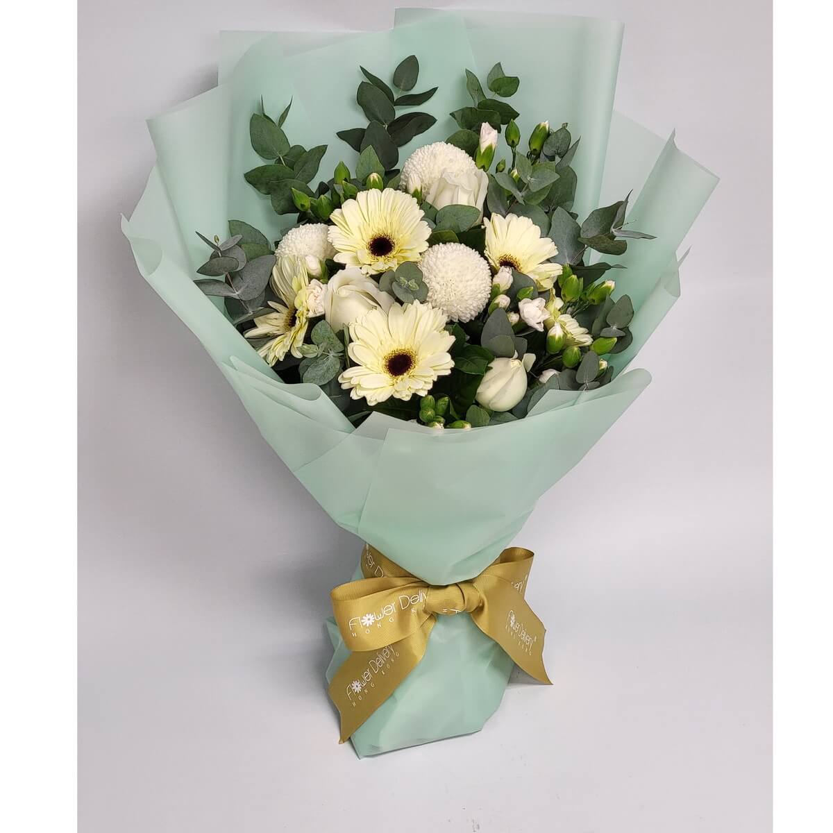 A soft white and green bouquet featuring cream gerberas, round white chrysanthemums, lisianthus, and eucalyptus leaves, wrapped in mint green paper with a golden yellow ribbon. 清新白花與尤加利葉交織,氣質典雅。