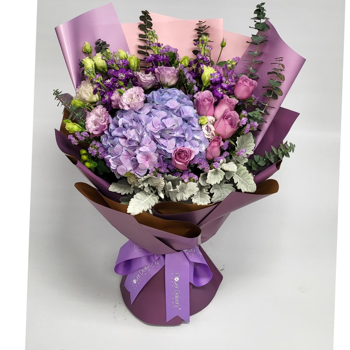 Arrangement of purple hydrangea, pink roses, lavender 洋桔梗, dusty miller, statice, and foliage in layered mauve and pink wrapping – 紫陽花、粉玫瑰、淡紫洋桔梗、銀葉、小花與葉材,粉紫層次包裝花束