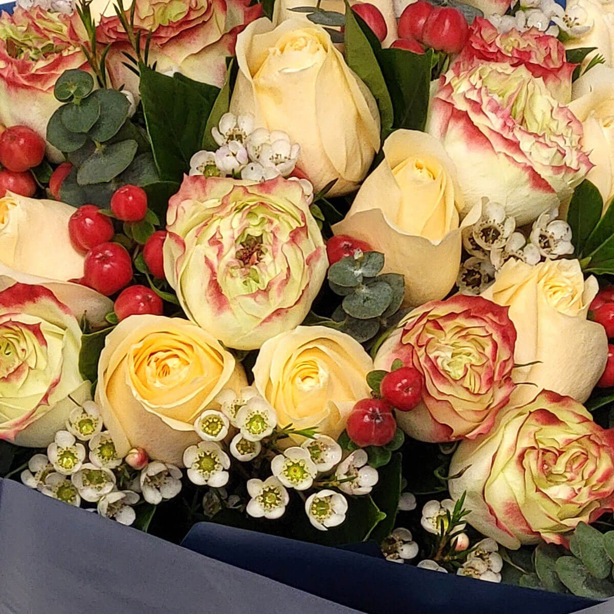 A festive bouquet of champagne roses, red-tipped blooms, red berries, white waxflowers, and lush greenery 香檳玫瑰與紅邊花朵、紅果與白蠟花交織,展現溫暖與喜悅的節慶氣息。