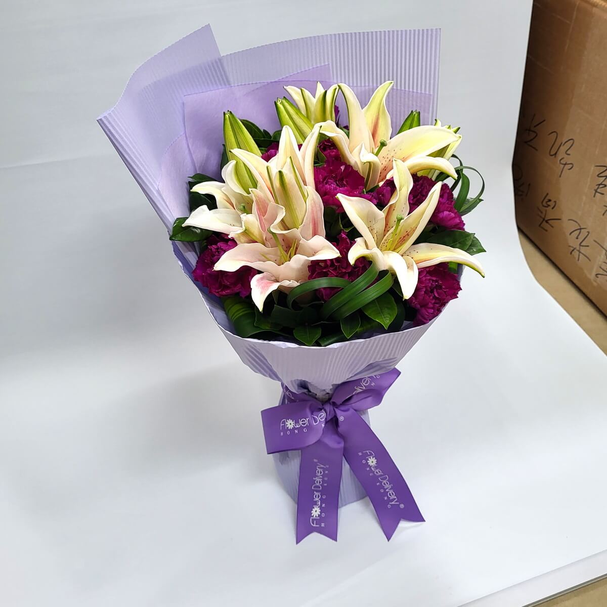 Elegant bouquet of pale peach lilies and deep magenta carnations, wrapped in soft lavender paper with a matching purple ribbon. 米杏百合搭配洋紅康乃馨,淡紫包裝高貴大方,散發優雅氣質。