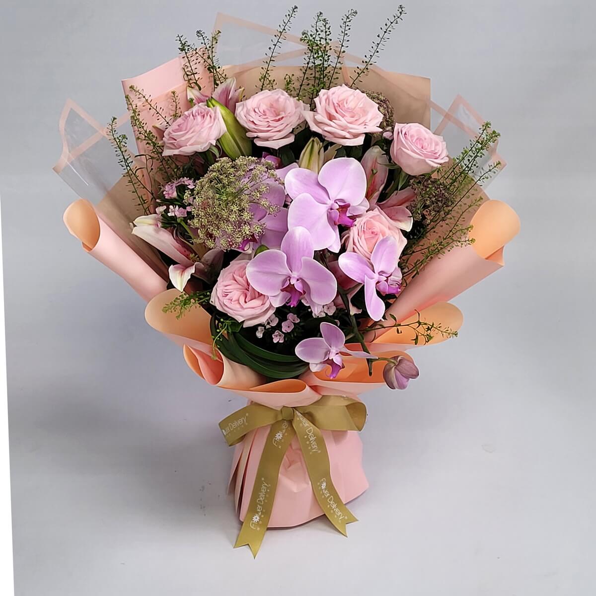 Blush pink roses and soft purple orchids with delicate greenery, wrapped in peach and pink paper with a golden ribbon. Graceful and romantic. 粉紅玫瑰與淺紫蝴蝶蘭搭配細葉與蜜桃包裝,溫柔婉約,充滿浪漫氛圍。