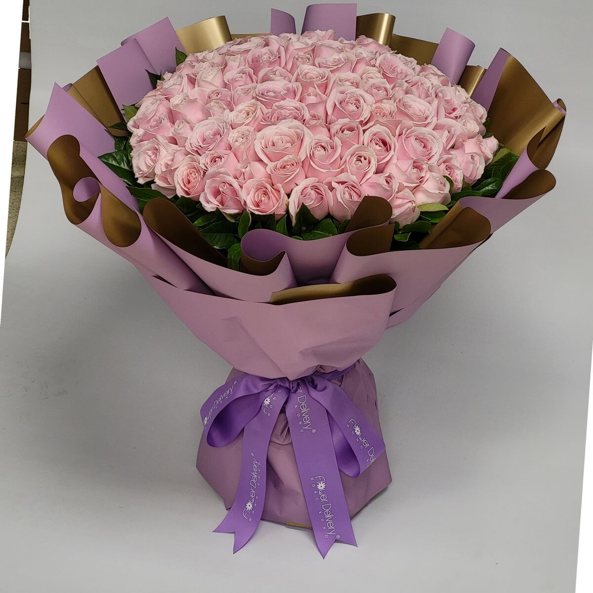 Lush bouquet of soft pink roses wrapped in lavender and gold paper with a violet ribbon. Feminine, delicate, and full of charm. 淡粉紅玫瑰花束,配紫金包裝與紫絲帶,柔美迷人。