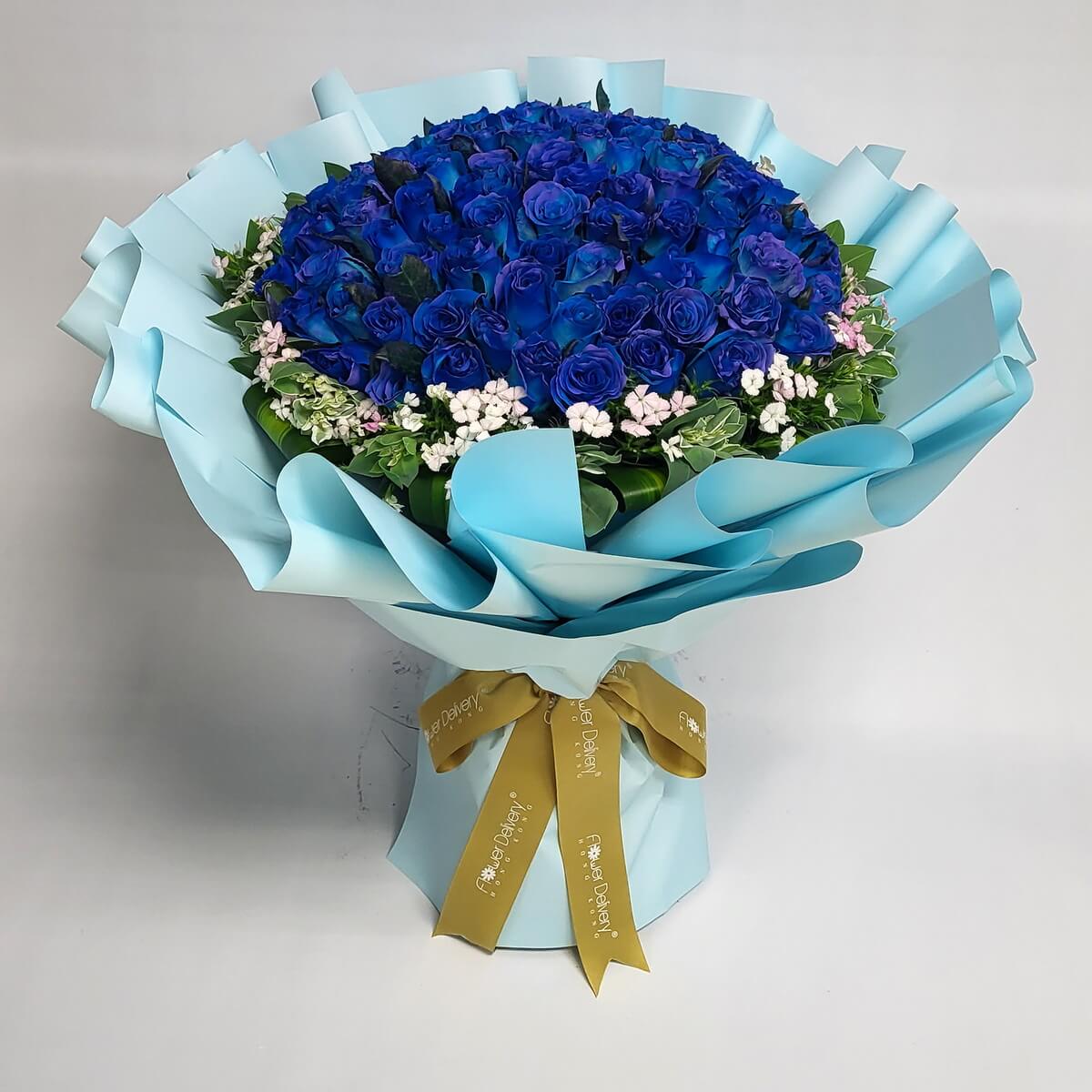 Stunning bouquet of vivid royal blue roses surrounded by white and light pink flowers, wrapped in light blue paper with a champagne ribbon. 鮮豔寶藍玫瑰花束,點綴粉白小花,配天藍包裝紙與香檳金絲帶,冷艷迷人。