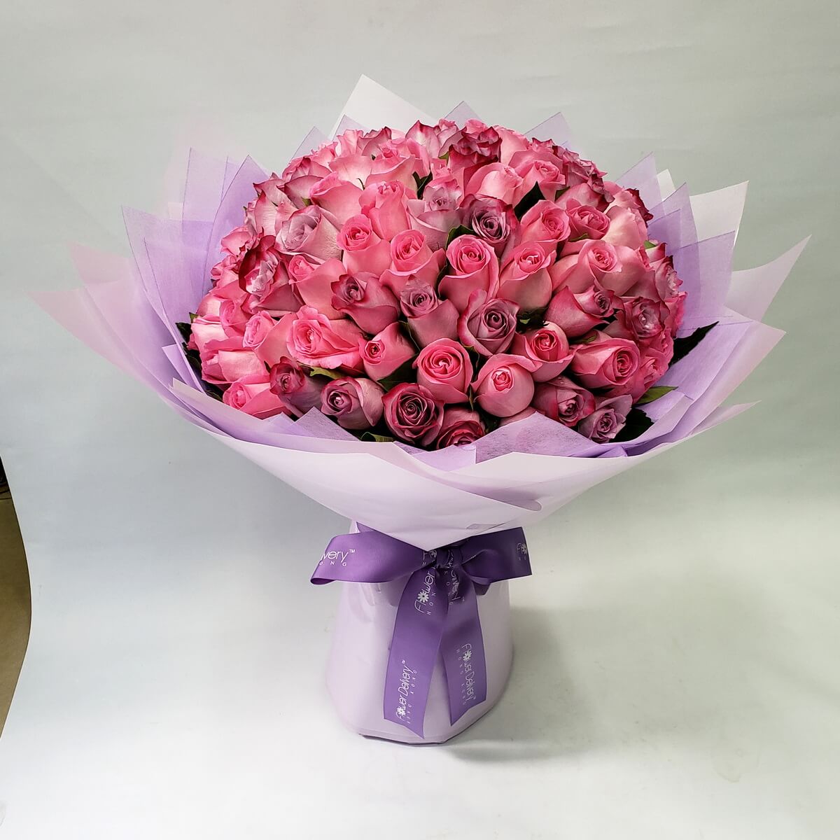 Large round bouquet of pink and lavender roses, wrapped in layers of soft lilac and white paper with a matching purple ribbon. 夢幻粉紫玫瑰花束,層次感包裝紙配襯紫色絲帶,浪漫高雅。