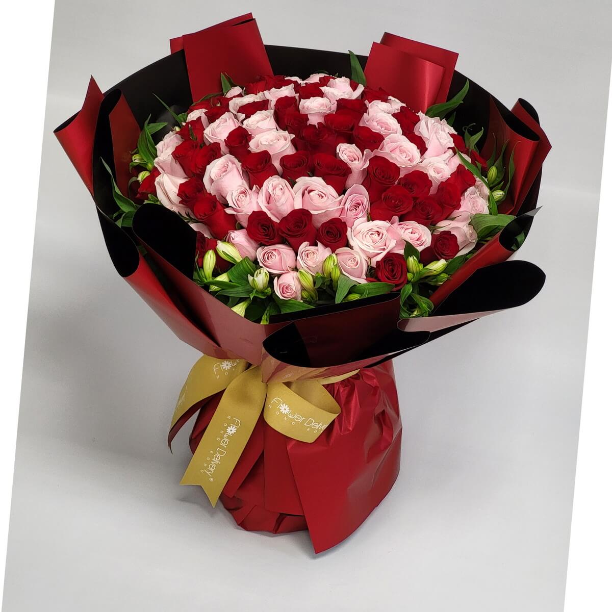 Luxurious round bouquet of red and pink roses arranged in a heart shape, wrapped in glossy red and black paper with a gold ribbon. 華麗心形紅粉玫瑰花束,圓形設計配紅黑光面包裝紙及金絲帶。