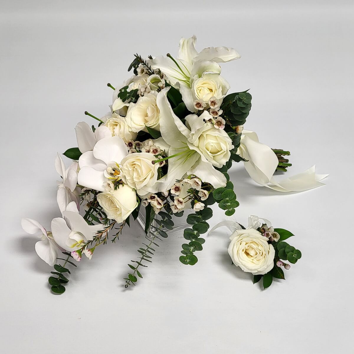 Elegant cascading bridal bouquet with white roses, lilies, orchids, wax flowers, and eucalyptus, paired with a matching boutonniere. 高雅垂墜式新娘花球,白玫瑰、百合、蝴蝶蘭、蠟花與尤加利葉搭配,同款襟花相襯。