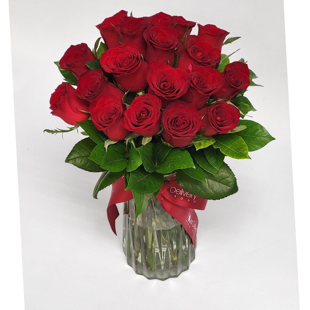 Elegant bouquet of long-stemmed red roses in a scalloped glass vase, accented with lush greenery and tied with a deep red ribbon. 高雅長枝紅玫瑰花束,搭配濃綠葉片,插於波紋玻璃瓶中,綁上深紅緞帶,展現經典浪漫氛圍。