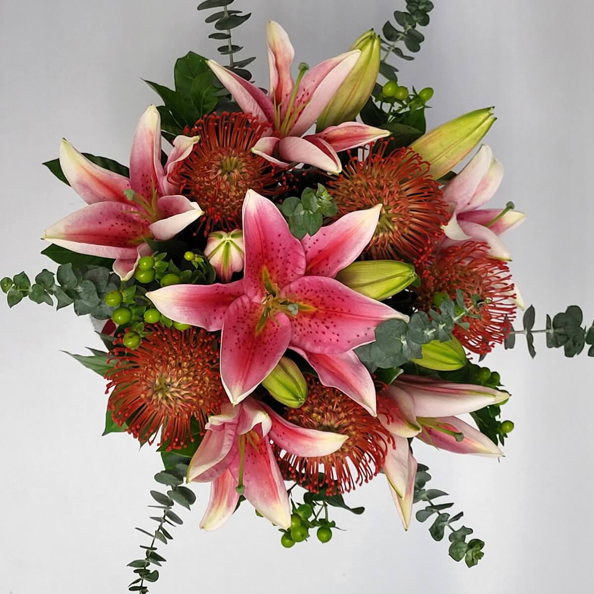 Top view of floral bouquet with pink oriental lilies, orange pincushion proteas, green hypericum berries and spiraled eucalyptus foliage - 粉紅東方百合、橙色針墊花、綠色小漿果及螺旋形尤加利葉組成的花束顶視圖