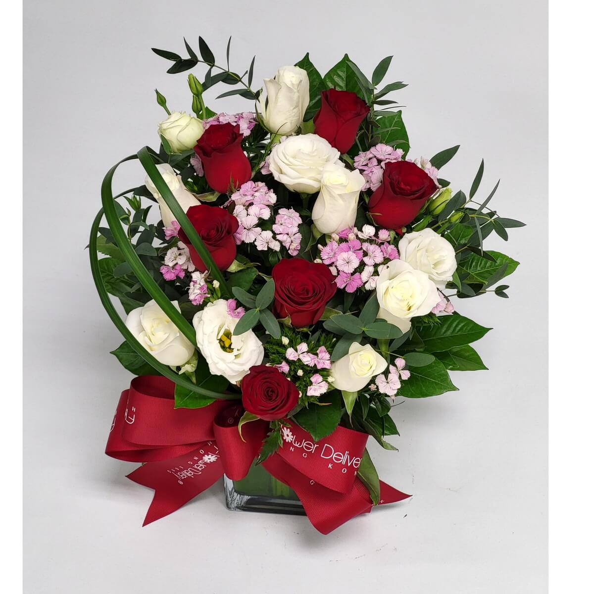 Red and white rose elegance 紅白玫瑰相間,粉色小花點綴,綠葉豐盈,配方形玻璃瓶與紅絲帶,展現經典浪漫與細膩情感的完美花藝設計。